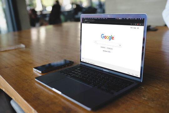 Bangkok, Thailand. June 27, 2026; A MacBook Pro laptop displaying the Google search engine homepage is placed on a wooden table next to a smartphone.