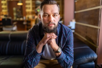 Obraz premium Man waiting on a leather sofa inside cozy salon interior