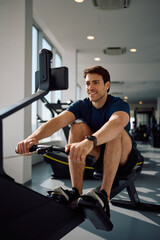 Obraz premium Happy sportsman exercising on rowing machine during gym workout.
