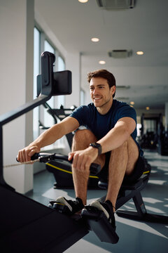 Happy sportsman exercising on rowing machine during gym workout.