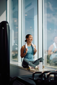 Happy Korean sportswoman by the window during water break in health club.