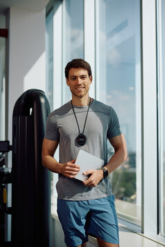 Happy personal coach with touchpad in health club looking at camera.