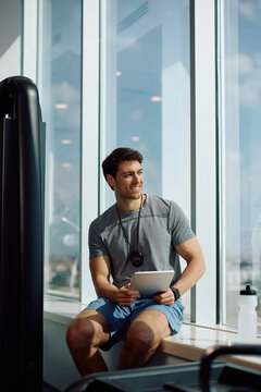 Happy fitness instructor using digital tablet in gym.