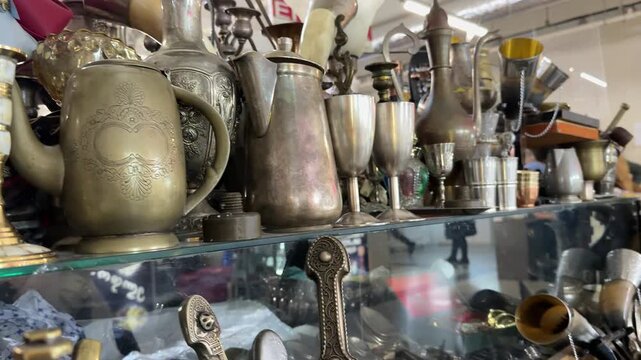 Antiques tableware metal, vintage brass and silver decorative objects displayed on store shelves in a rustic interior for antique collectors and home decor