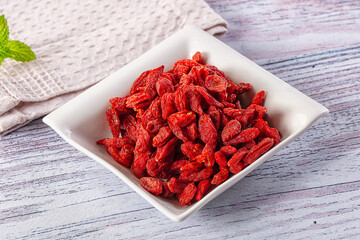 Red goji berries in white ceramic bowl on rustic wooden surface with mint leaf and linen cloth © Andrei Starostin