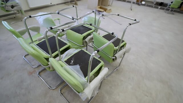 Chrome office seats sit upside down with protective plastic film during renovation. Clean minimalist space provides organized workspace feel