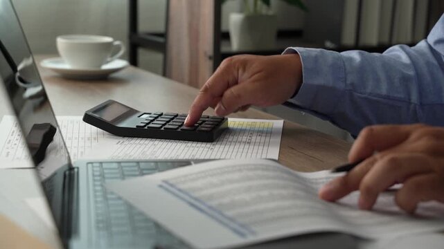 man use calculator while holding a financial document beside a laptop, showing budgeting, accounting, and report review workflow for corporate finance planning process.