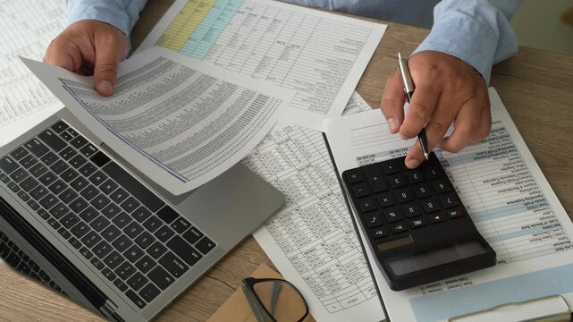 man use calculator while holding a financial document beside a laptop, showing budgeting, accounting, and report review workflow for corporate finance planning process.