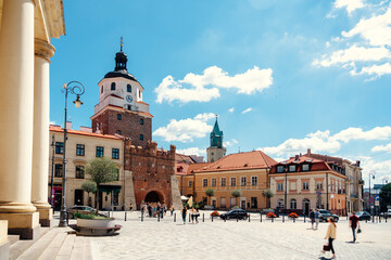 Obraz premium The historic Kraków Gate stands prominently as the gateway to the charming, sunlit Old Town square in Lublin, Poland.