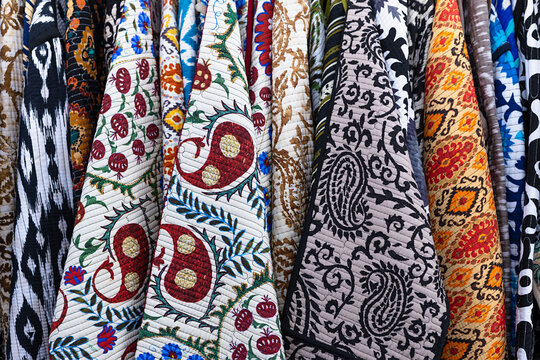 Traditional Uzbek textiles with suzani and ikat patterns hanging at Siab bazaar in Samarkand. Colorful quilted fabrics with pomegranate and paisley motifs ideal for travel and craft content.