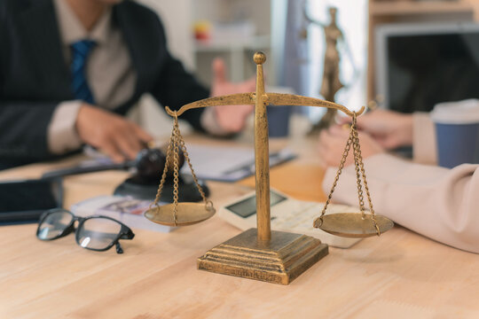  Close up of hands signing legal paper with gavel, scales of justice, and lady justice statue on desk. Law, justice, and agreement concept.