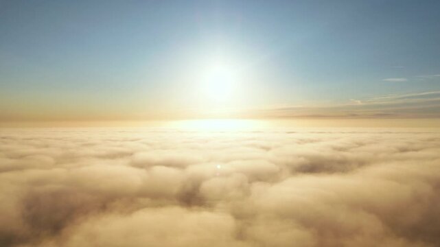Golden sunset shining above fluffy clouds in peaceful sky.
