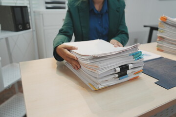 An office employee standing behind a light wooden desk uses both hands to lift and vertically align...