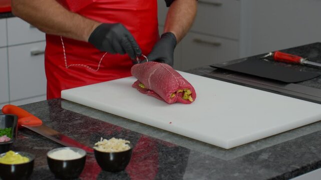 Professional chef preparing and tying a stuffed meat roll on a kitchen worktop. Culinary craftsmanship, food preparation, cooking process, hospitality, and gourmet cuisine concepts
