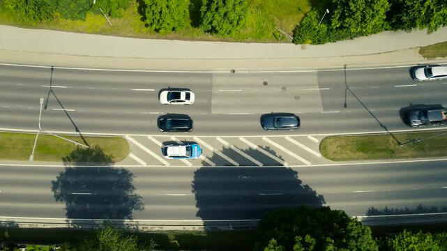 Aerial top down view of a police car parked in a safety zone on a busy city highway, monitoring traffic and using radar to check for speeding vehicles as cars drive by on a sunny day
