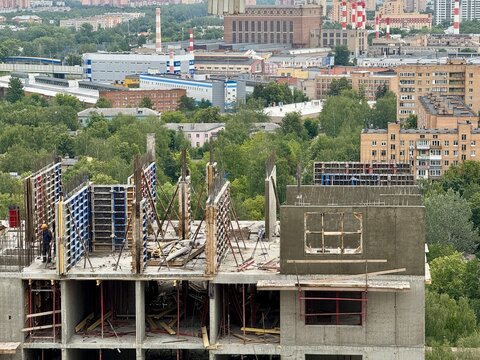 Construction site building construction, in urban area with industrial buildings and greenery in, with concrete structures, scaffolding, construction materials, worker, with gray, blue accents.
