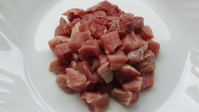 Closeup of uncooked raw meat diced into small cube cut pieces isolated inside white plate background. Minced fillet of cow, pork, beef, lamb or mutton light red meat. Healthy protein diet concept.