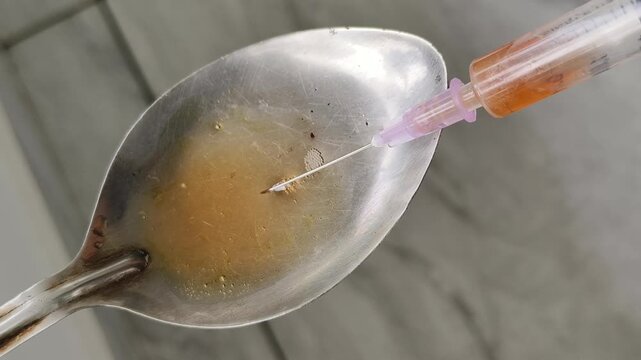 Needle closeup filling dissolved heroin or brown sugar drug liquid inside syringe from spoon for ecstasy intoxication injection. Cocaine and meth narcotic substance addiction and consumption concept.