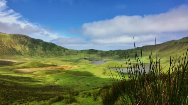 Clouds drift over lush volcanic caldera with lakes and grassy slopes in daylight