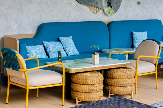 Blue sofa, yellow chairs, woven stools, and a marble table. Cozy cafe corner, bright and inviting. Light gray walls, minimalist decor. Perfect for casual meetings or relaxed gatherings