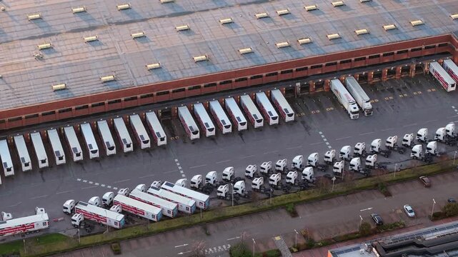 Overhead drone tracking shot of a modern freight logistics compound with delivery trucks at cargo docks.