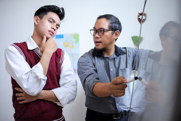 Obraz premium male Teacher with Glasses Explaining Lesson on Whiteboard to Thoughtful Young male Student in Class