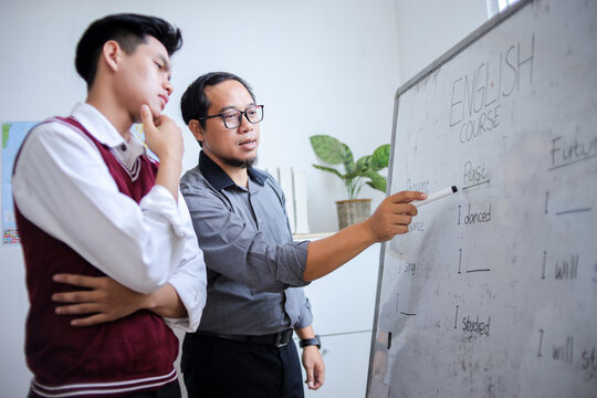 Asian Teacher Pointing at Whiteboard While Explaining an English Grammar Rule to Thoughtful Student