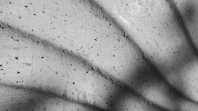 Water flows down a vertical embossed stone wall in close-up. Tiny bubbles and droplets create a moving abstract grey pattern. The minimalist relief water feature serves as modern interior decor.