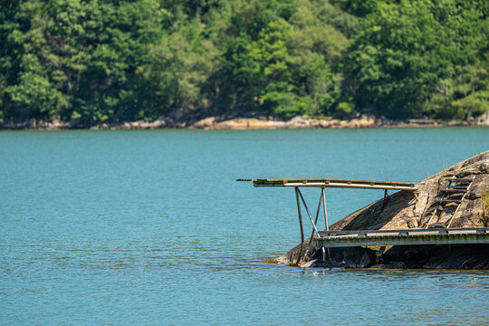 Wooden lakeside jetty on rocky shoreline under summer daylight.