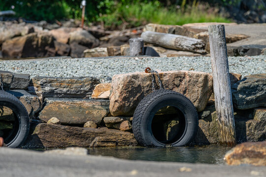 Stone shoreline with weathered posts and tire bumpers by the water edge.