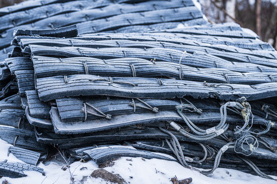 Stack of worn rubber conveyor belts with steel cables in snow.