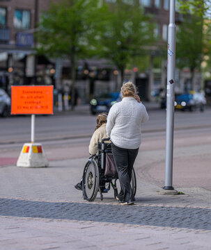 Caregiver assisting wheelchair user along quiet urban sidewalk.