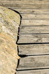 Fototapeta premium Weathered wooden boardwalk beside rough coastal rock texture.