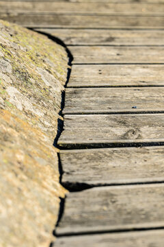 Weathered wooden boardwalk beside rough coastal rock texture.