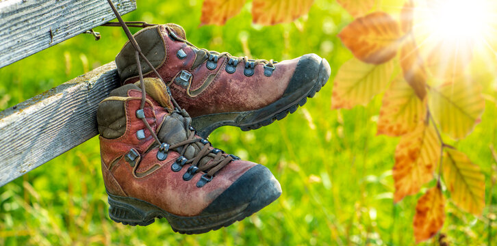 Ein Paar Wanderstiefel aus Leder h&auml;ngen mit Herbstlaub an einem h&ouml;lzernen Zaun  im Allg&auml;u - FOTOMONTAGE