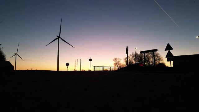 Wind Turbines Silhouette with Car Traffic at Sunset. Renewable Green Energy and Sustainable Technology Concept.