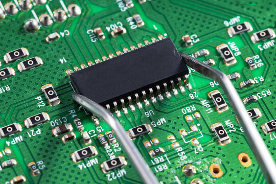 Technician  using tweezers to work on a green circuit board.