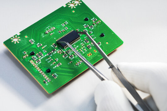 Close-up of gloved hand using tweezers to handle a microchip. Electronics repair.