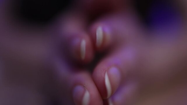 Detailed close-up shot of a woman's fingers and nails under moody, soft lighting with purple hues. Macro focus highlights texture and natural beauty in an intimate, serene moment.