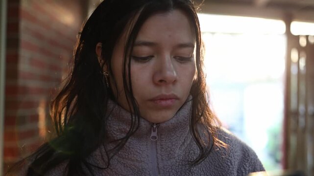 A young Latina woman in a cozy lavender fleece browses her smartphone outside, framed by golden hour sunlight, soft focus, and warm tones for a candid, relatable lifestyle moment.
