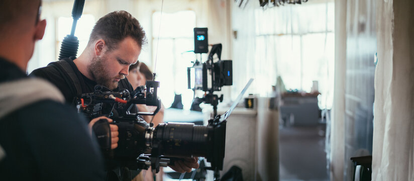 The director of photography with a camera on the set. A professional videographer is working on filming a movie or commercial for a TV series. The filming process takes place indoors in a studio.