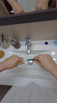 Man squeezing toothpaste on brush in bathroom sink pov