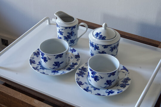 Porcelain tea set with blue floral pattern serving cups, creamer, and sugar bowl on a cart
