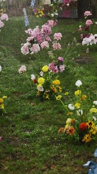 Vertical video. Rain falls on outdoor wedding decor with flower arrangements on a forest lawn.