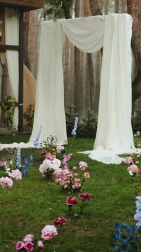 Vertical video. Rain falls on an outdoor wedding arch with flower decorations in a forest setting.