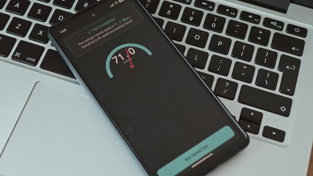 Close up of a hand tapping a smartphone screen to run a network speed test on a laptop background
