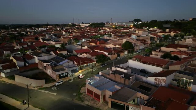 Aerial view of a residential neighborhood at dusk with red tiled roofs and streetlights illuminating the roads