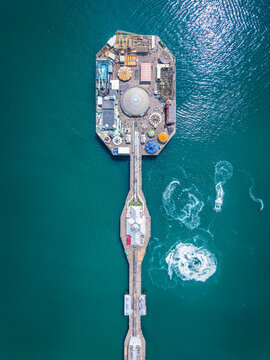 Aerial overhead view of the famous Brighton Pier in East Sussex, England, with public amusement park over emerald ocean