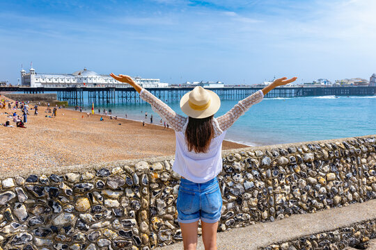 Rear view of a happy woman looking at the beach and famous beach and Pier of Brighton, East Sussex, England, during a sunny summer day