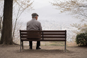 Fototapeta premium 公園のベンチに一人で座る孤独なシニア男性。アジア人、日本人